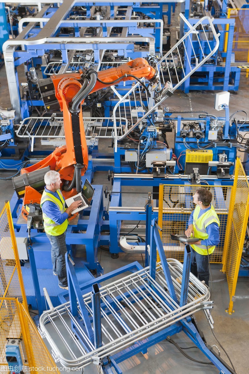 工人们观看机械机械在制造工厂的生产线上吊起钢铁围栏